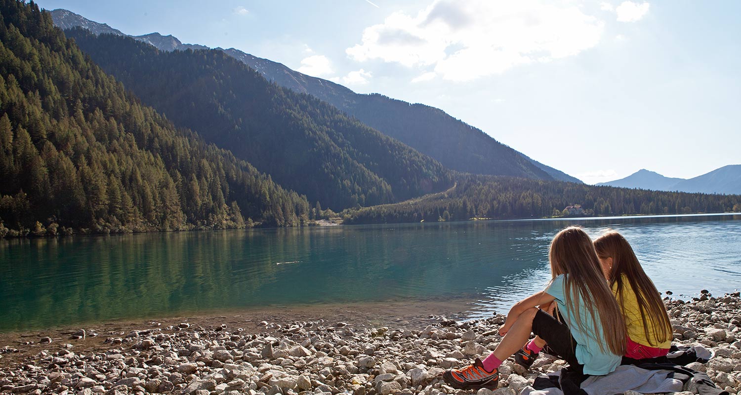 Two girls sitting on the lake shore with mountains at the back
